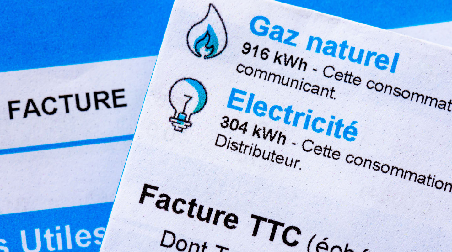 Syndic professionnel analysant plusieurs propositions tarifaires de fournisseurs de gaz étalées sur son bureau, avec écran affichant un tableau comparatif en français, dans un bureau d'agence contemporain